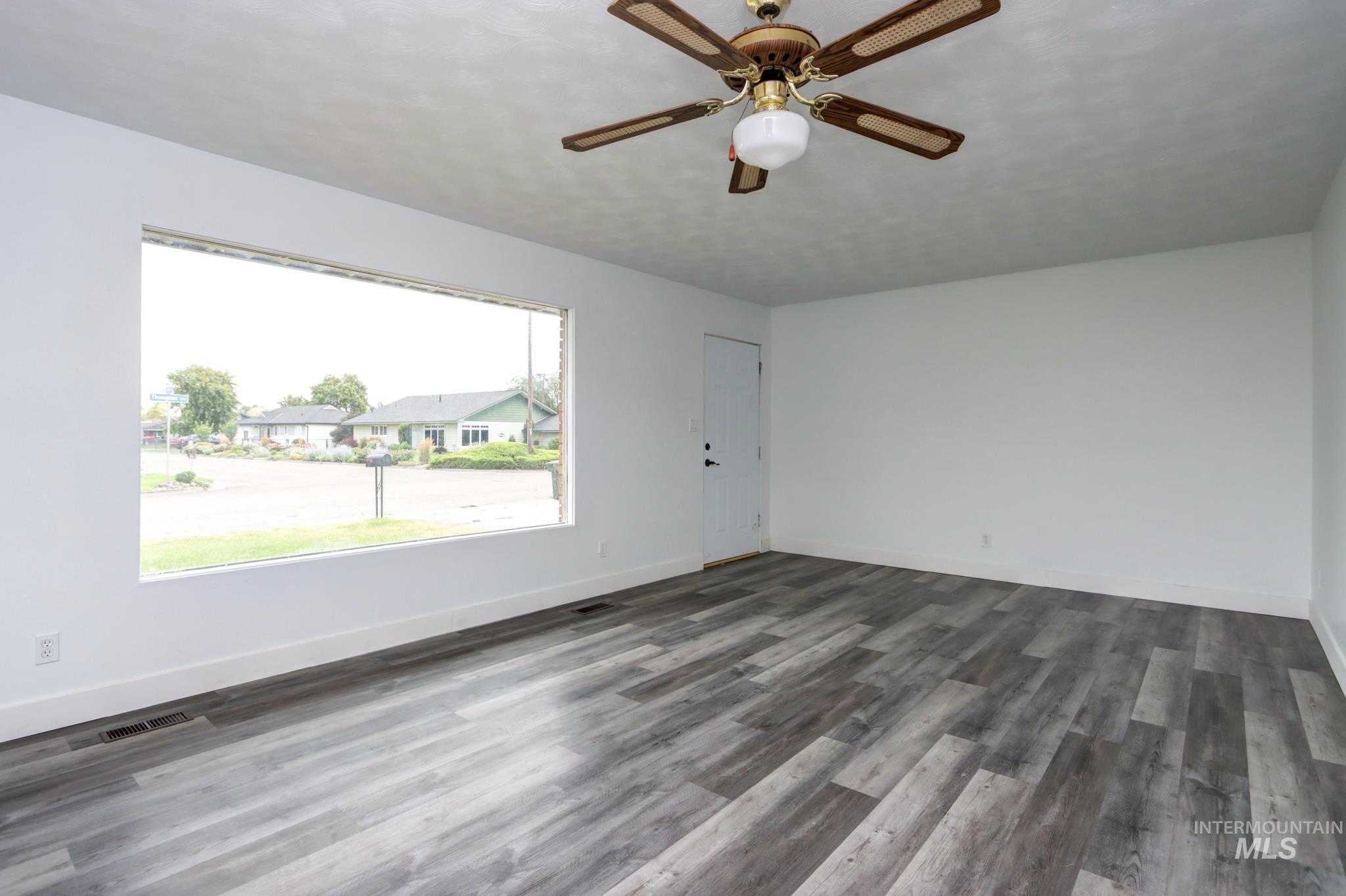 801 Thompson Avenue Nyssa, OR 97913 - Photo 3 of 46 Bright interior space featuring a large picture window, wood-finish flooring, a ceiling fan with integrated lighting, a white painted door, and crisp white walls