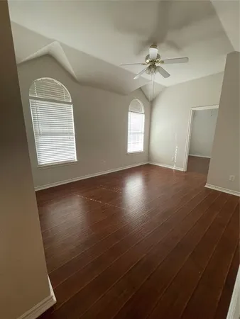 an empty room with wooden floor fan and windows