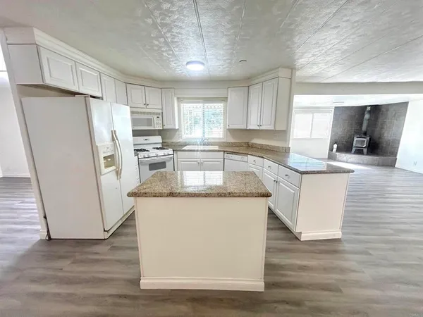 a kitchen with stainless steel appliances granite countertop a refrigerator a stove a sink and white cabinets with wooden floor