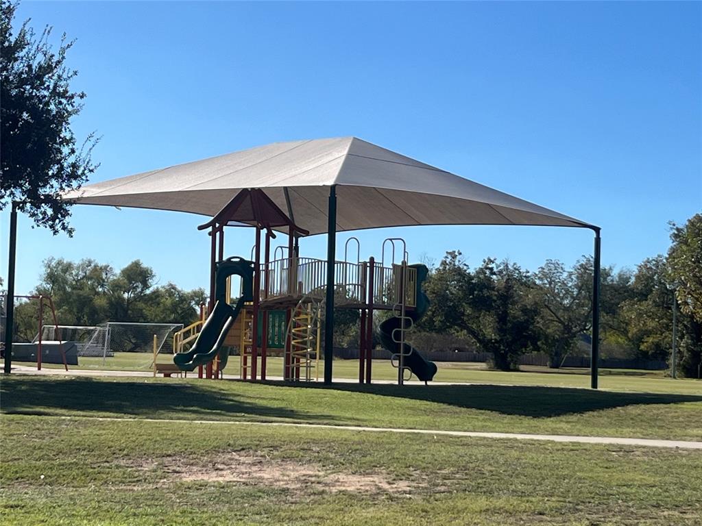 617 Barbara Way Bastrop, TX 78602 - Photo 18 of 20 A vibrant playground structure with slides and climbing areas sits under a broad shade canopy on a sunny day.