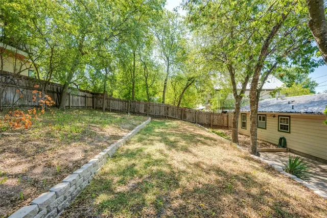 a backyard of a house with lots of plants and large trees