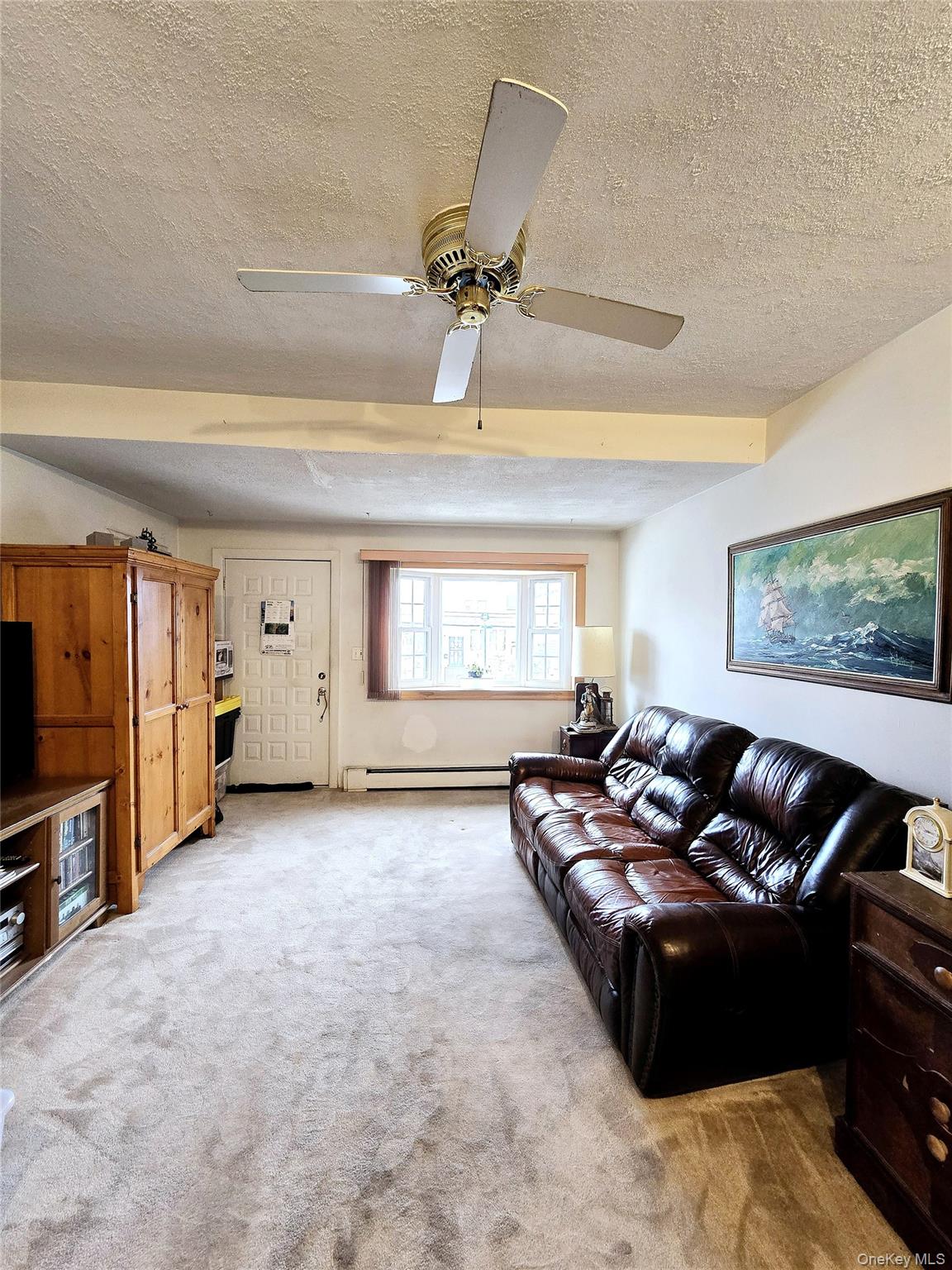 85-09 Sutter Avenue Queens, NY 11417 - Photo 5 of 12 Living room with light carpet, baseboard heating, a ceiling fan, and a textured ceiling
