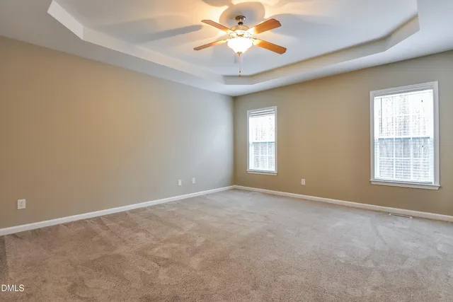an empty room with a chandelier fan and windows