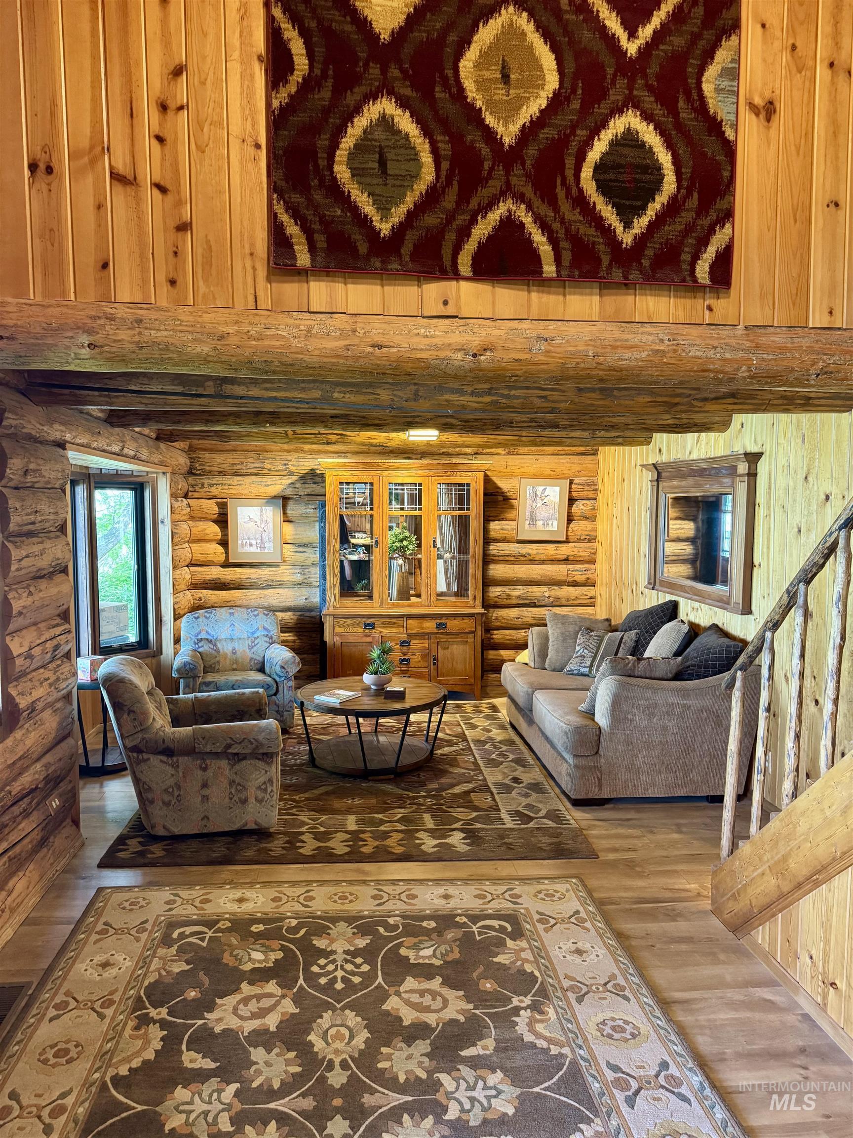 62 Bell Rapids Road Hagerman, ID 83332 - Photo 9 of 34 Living area featuring log walls, exposed wood beams, wood-finish flooring, and a prominent built-in wood cabinet with glass doors