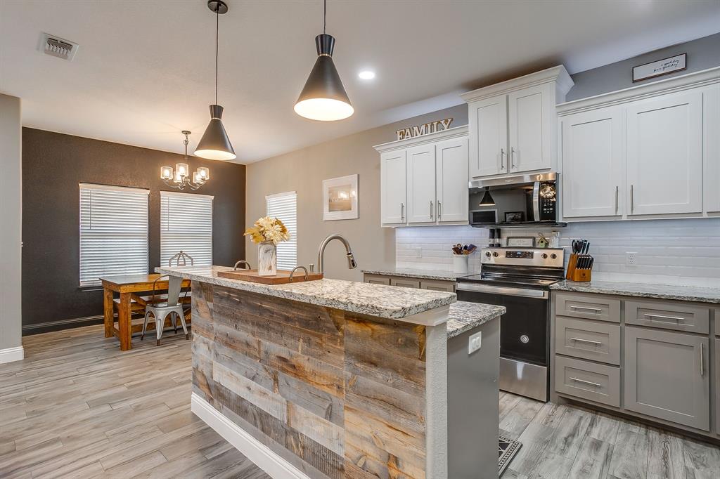 409 Titus Drive Springtown, TX 76082 - Photo 14 of 39 a kitchen with stainless steel appliances granite countertop a stove top oven a sink a dining table and chairs with wooden floor