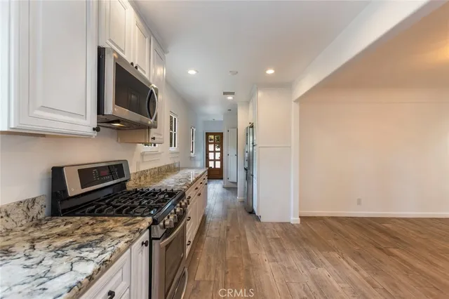 a kitchen with stainless steel appliances granite countertop a stove top oven a sink dishwasher and a refrigerator with wooden floor