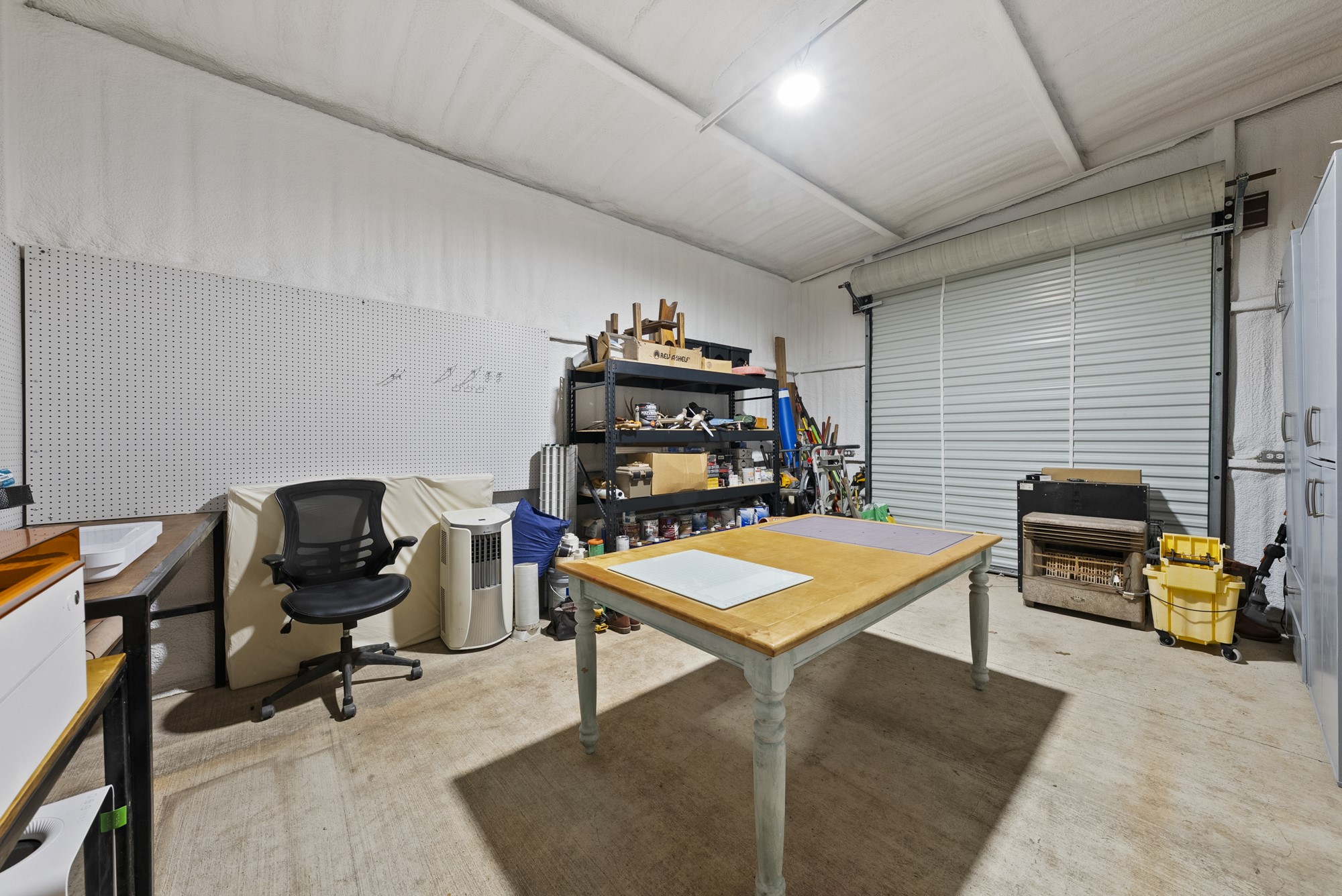 2802 Robin Road Manchaca, TX 78652 - Photo 27 of 40 Versatile garage space featuring a large roll-up door, exposed ceiling structure, concrete flooring, and extensive pegboard wall