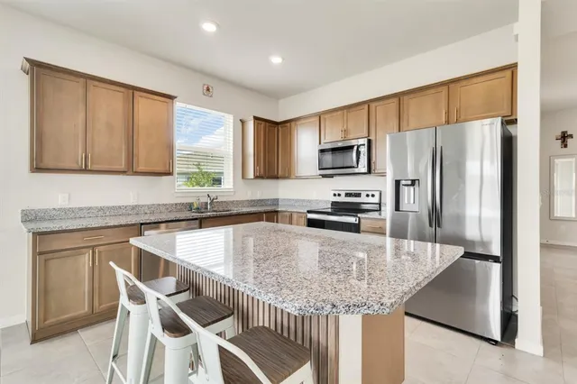 a kitchen with kitchen island granite countertop stainless steel appliances a sink stove refrigerator and a window