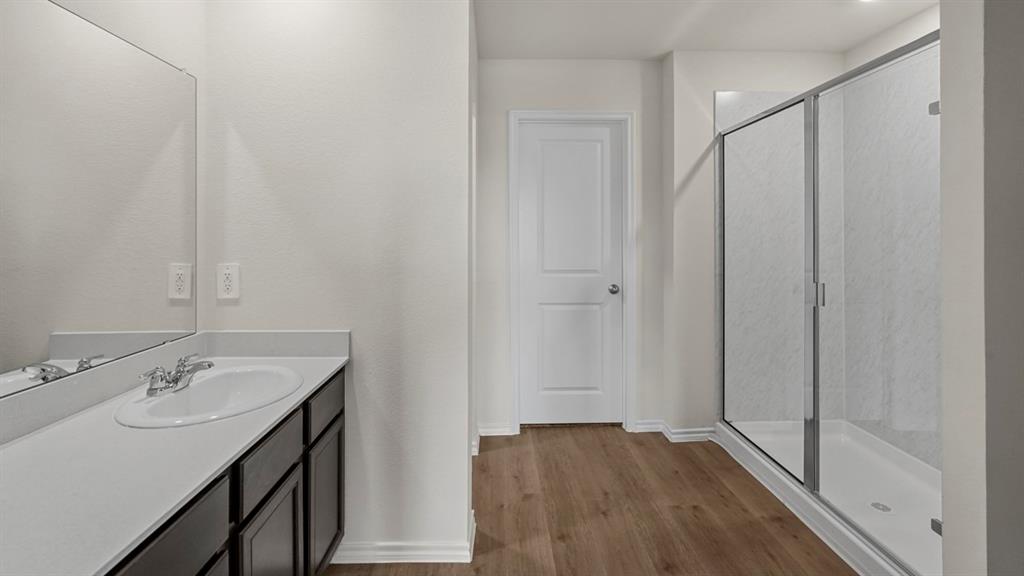 1969 Freeman Street Tyler, TX 75704 - Photo 16 of 30 Bathroom featuring a vanity with an integrated sink, a rectangular mirror, wood-finish flooring, a white paneled door, and a glass-enclosed shower