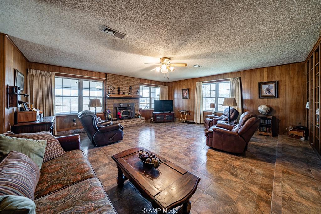 1992 Sand Flat Road Jacksboro, TX 76458 - Photo 23 of 36 Living room featuring a brick fireplace, a textured ceiling, ceiling fan, and wood walls