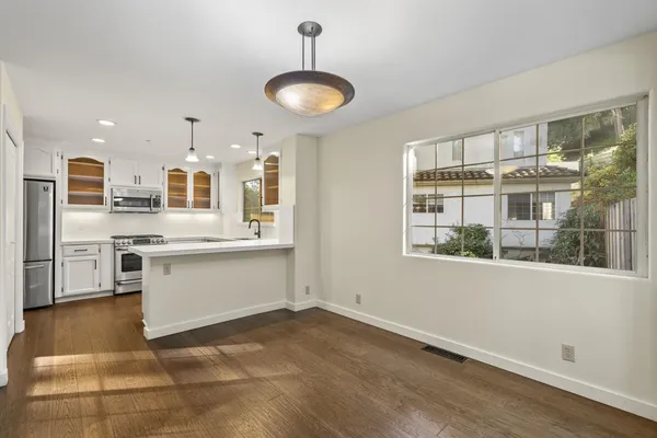 a kitchen with stainless steel appliances granite countertop a stove a sink dishwasher a refrigerator and a dining table with wooden floor