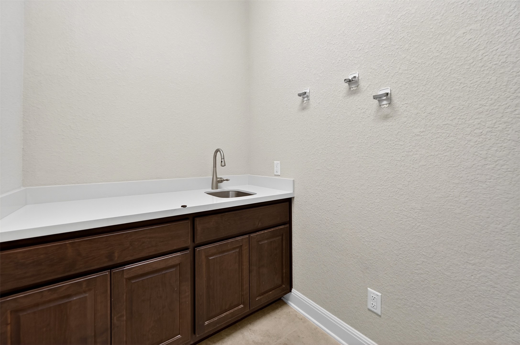 1201 Positano Pass Leander, TX 78641 - Photo 15 of 40 Utility area featuring a stainless steel sink with a high-arch faucet, a white countertop, and dark wood-finish cabinetry