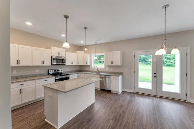 a kitchen with stainless steel appliances granite countertop a refrigerator a sink dishwasher a stove and white cabinets with wooden floor