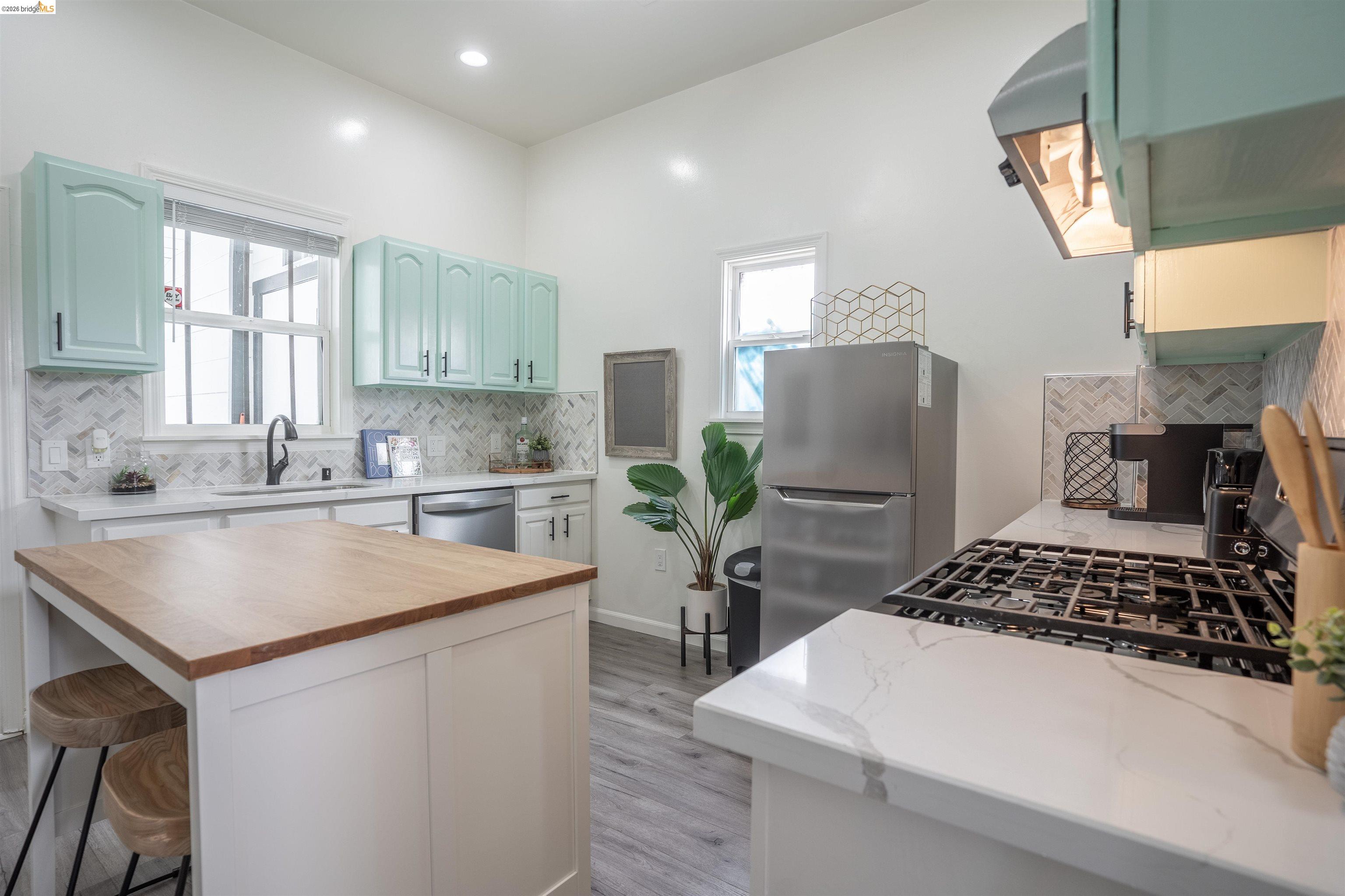 527 Chester Street Oakland, CA 94607 - Photo 41 of 47 527 (Upstairs) Kitchen featuring butcher block counters, stainless steel appliances, a kitchen breakfast bar, light wood finished floors, and a center island