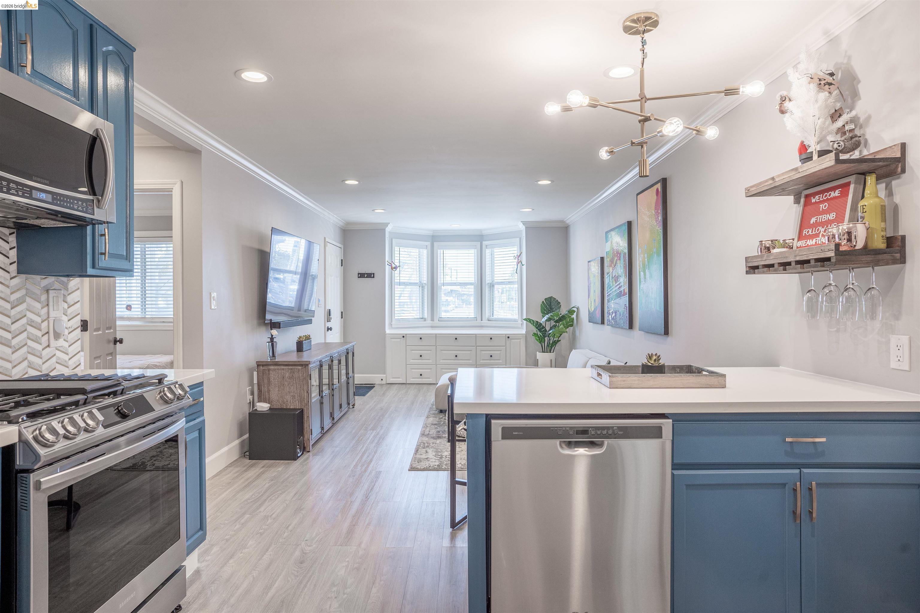 527 Chester Street Oakland, CA 94607 - Photo 6 of 47 525 (Downstairs) Kitchen with blue cabinetry, a peninsula, stainless steel appliances, backsplash, and ornamental molding