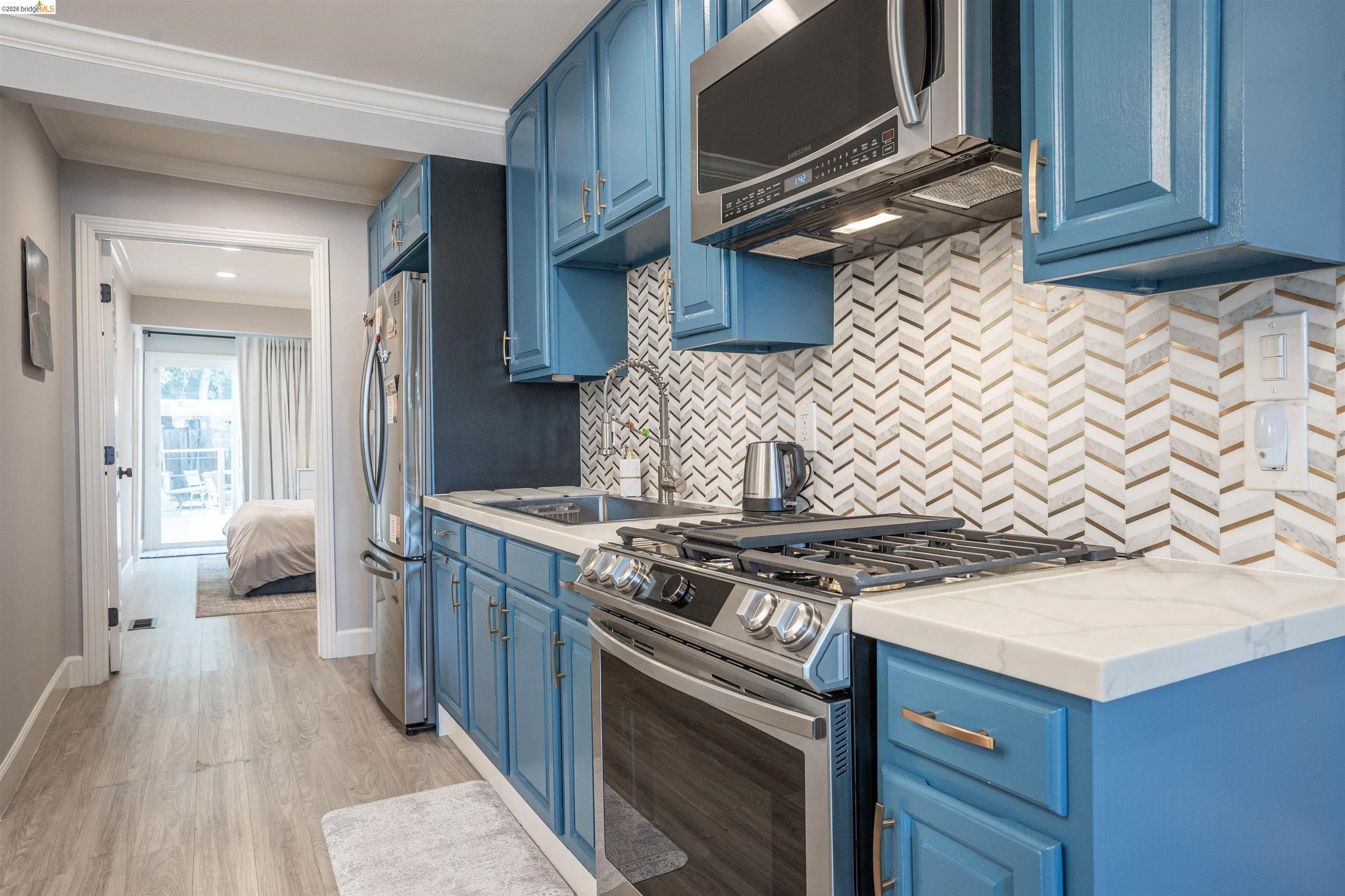 527 Chester Street Oakland, CA 94607 - Photo 9 of 47 525 (Downstairs) Kitchen featuring blue cabinets, stainless steel appliances, crown molding, light countertops, and light wood-style flooring
