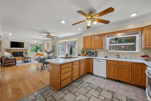 1726 Wasatch Boulevard Sandy, UT 84092 - Photo 11 of 38 Open-concept living area featuring a kitchen with wood cabinetry and tile flooring, a living room with wood-finish flooring, a brick-surround fireplace, and multiple windows