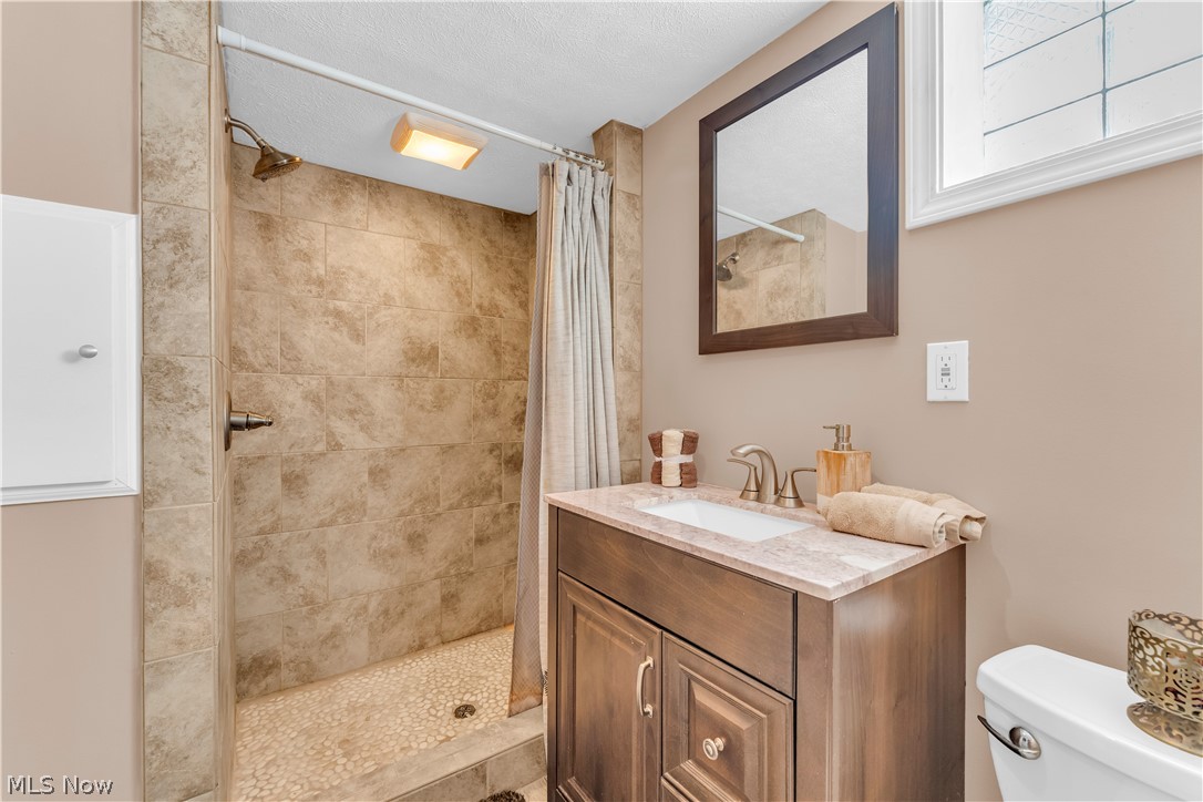 3023 Norris Avenue Cleveland, OH 44134 - Photo 33 of 41 Bathroom featuring a tiled walk-in shower with pebble flooring, a single vanity with a stone-finish countertop, and a framed mirror