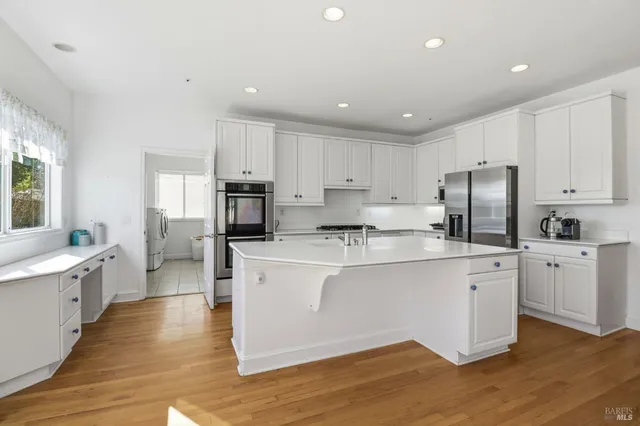 a large white kitchen with stainless steel appliances granite countertop a stove a sink a refrigerator and white cabinets with wooden floor