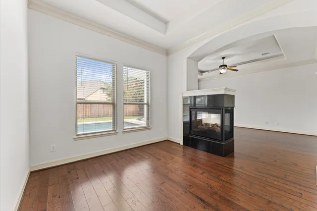 an empty room with wooden floor fire place and windows