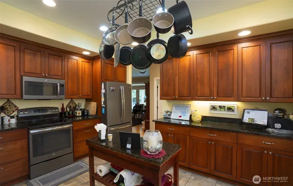 a kitchen with stainless steel appliances granite countertop a refrigerator a sink a stove and chairs with wooden floor