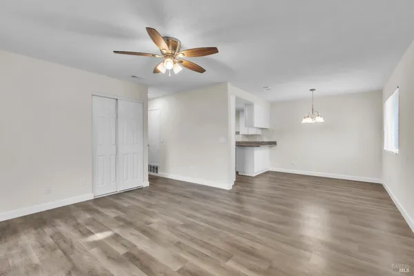 a view of an empty room with wooden floor and a ceiling fan