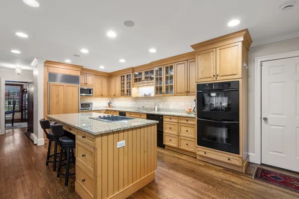 a kitchen with stainless steel appliances granite countertop a stove top oven a refrigerator a sink and a dining table with wooden floor