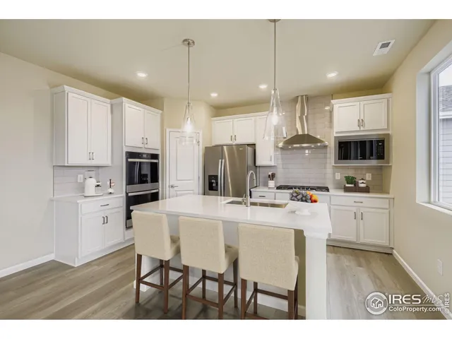 a kitchen with stainless steel appliances kitchen island granite countertop a refrigerator a stove top oven a sink dishwasher and white cabinets with wooden floor