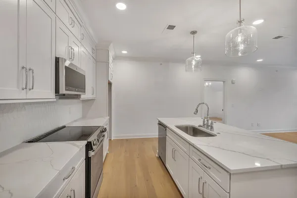 a kitchen that has a sink a microwave oven a stove and white cabinets with wooden floor