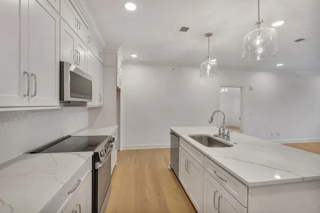 a kitchen that has a sink a microwave oven a stove and white cabinets with wooden floor