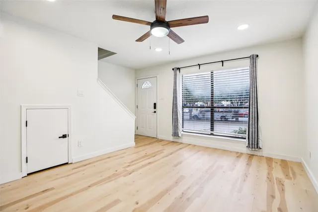 an empty room with wooden floor fan and windows