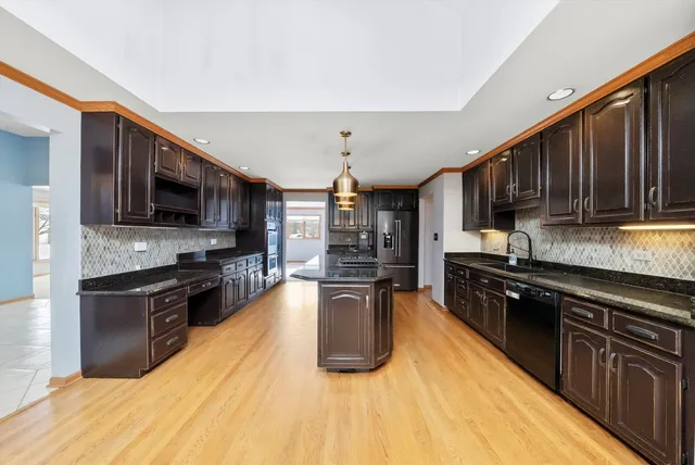 a kitchen with stainless steel appliances kitchen island granite countertop a stove top oven a sink dishwasher a dining table and chairs with wooden floor