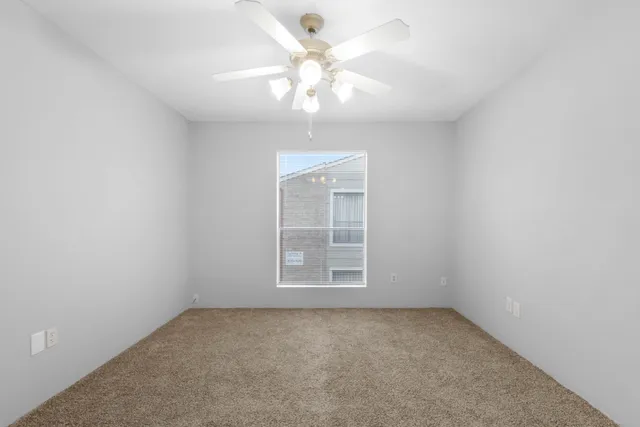 an empty room with a chandelier fan and windows