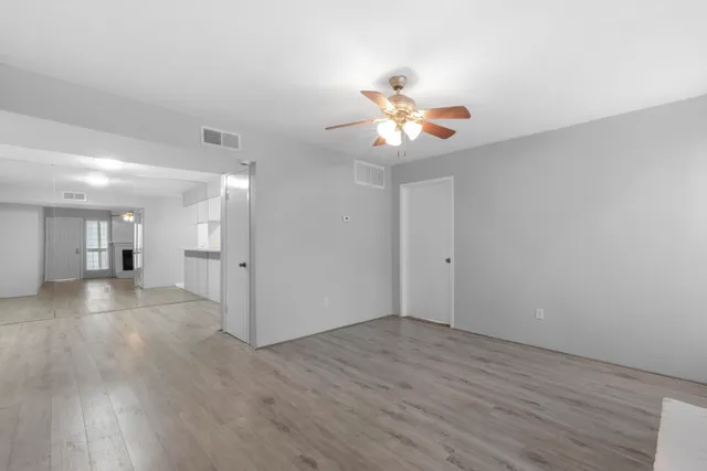 a view of an empty room with wooden floor and a ceiling fan