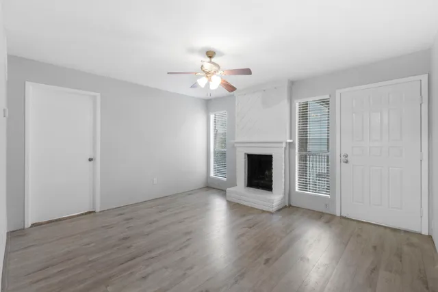 an empty room with wooden floor a chandelier fan and windows