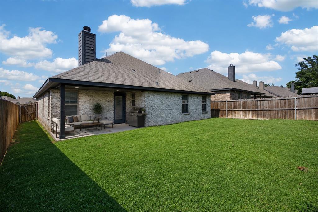 125 Maverick Lane Pilot Point, TX 76258 - Photo 25 of 28 Expansive green lawn with a covered patio, brick exterior, and dark trim details
