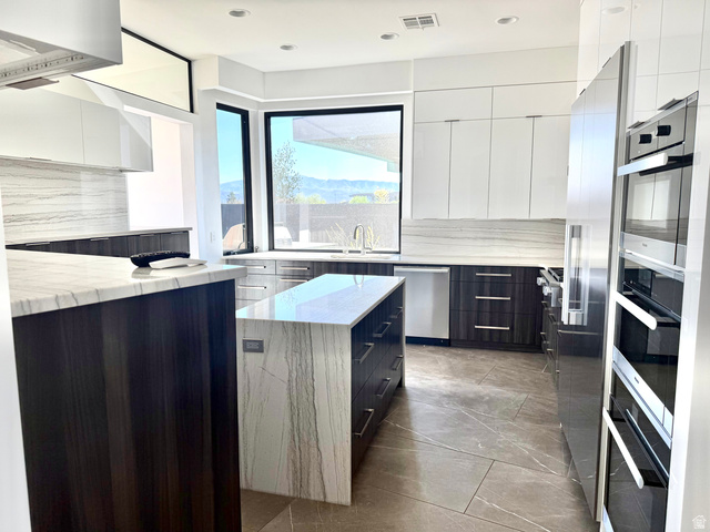 1500 Split Rock, Unit 150 Ivins, UT 84738 - Photo 9 of 18 Contemporary kitchen featuring a waterfall island with stone countertop, dark wood-finish cabinetry, integrated stainless steel appliances, and large windows