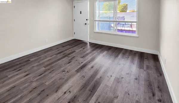 a view of an empty room with wooden floor and a window