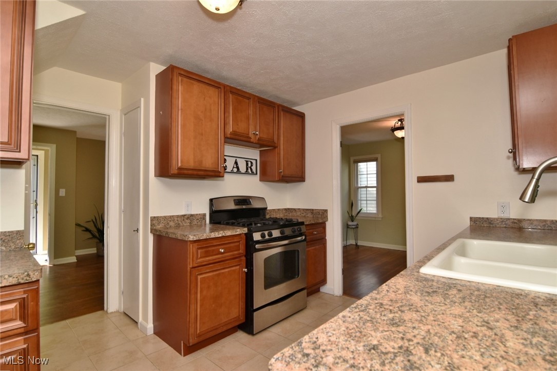 3679 Fenley Road Cleveland Heights, OH 44121 - Photo 17 of 45 Kitchen featuring stainless steel range with gas stovetop, brown cabinets, light tile patterned floors, and a textured ceiling