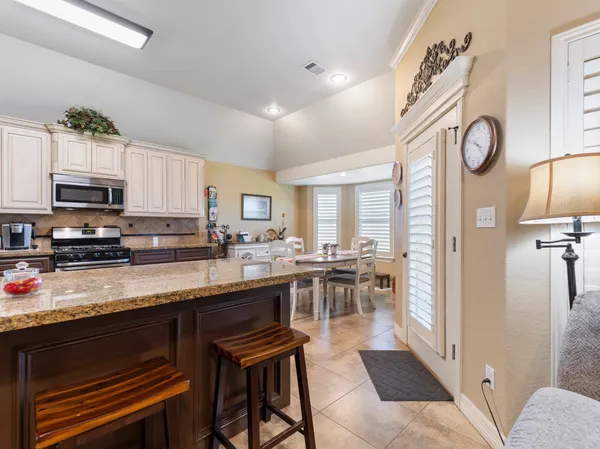 a kitchen with stainless steel appliances granite countertop a stove top oven a sink a dining table and chairs with wooden floor