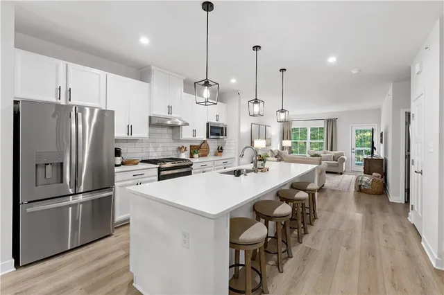 a kitchen with stainless steel appliances a refrigerator a stove a sink dishwasher a oven and a dining table with wooden floor