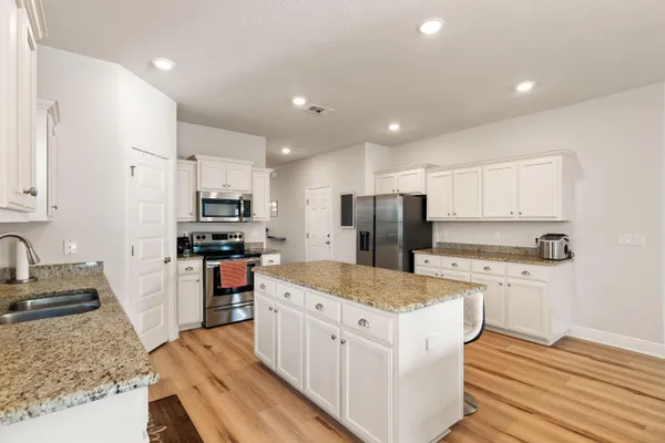 a kitchen with stainless steel appliances granite countertop a sink stove refrigerator and white cabinets with wooden floor