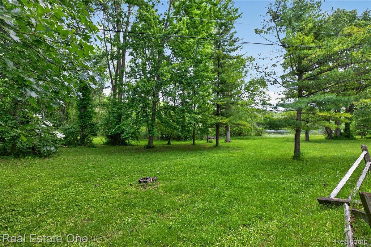 425 Courtney Road Leonard, MI 48367 - Photo 68 of 89 Expansive green lawn surrounded by mature trees, featuring a distant body of water and a rustic wooden fence