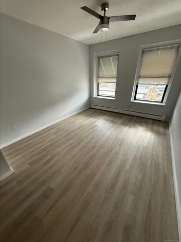 an empty room with wooden floor fan and windows