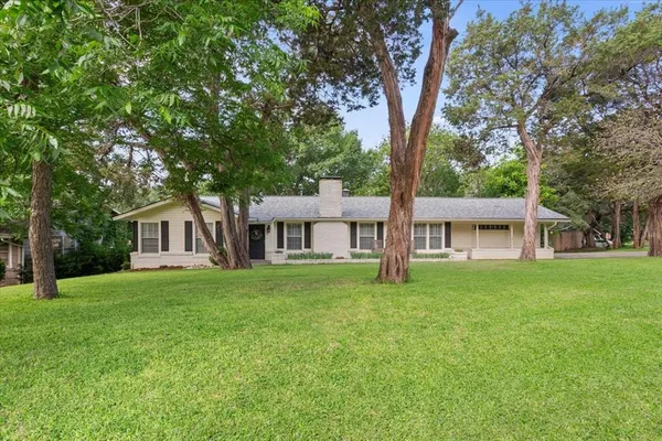 a house that is sitting in the grass with large trees and wooden fence