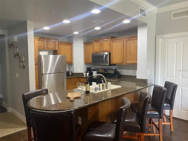 a kitchen with stainless steel appliances granite countertop a dining table chairs refrigerator and sink