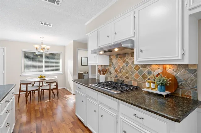 a kitchen with granite countertop a stove a sink a dining table and chairs with wooden floor