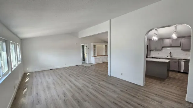 an empty room with wooden floor and a view of kitchen