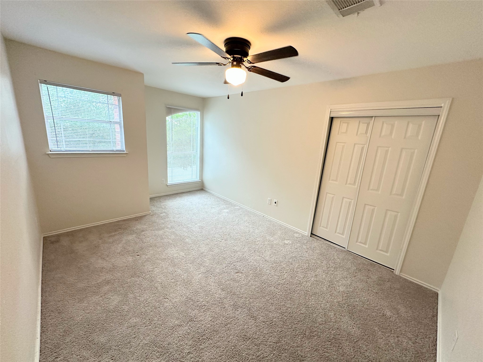 12929 Waynespur Lane Elgin, TX 78621 - Photo 15 of 20 The room features light-colored carpet flooring, two windows providing natural light, and a ceiling fan with integrated lighting