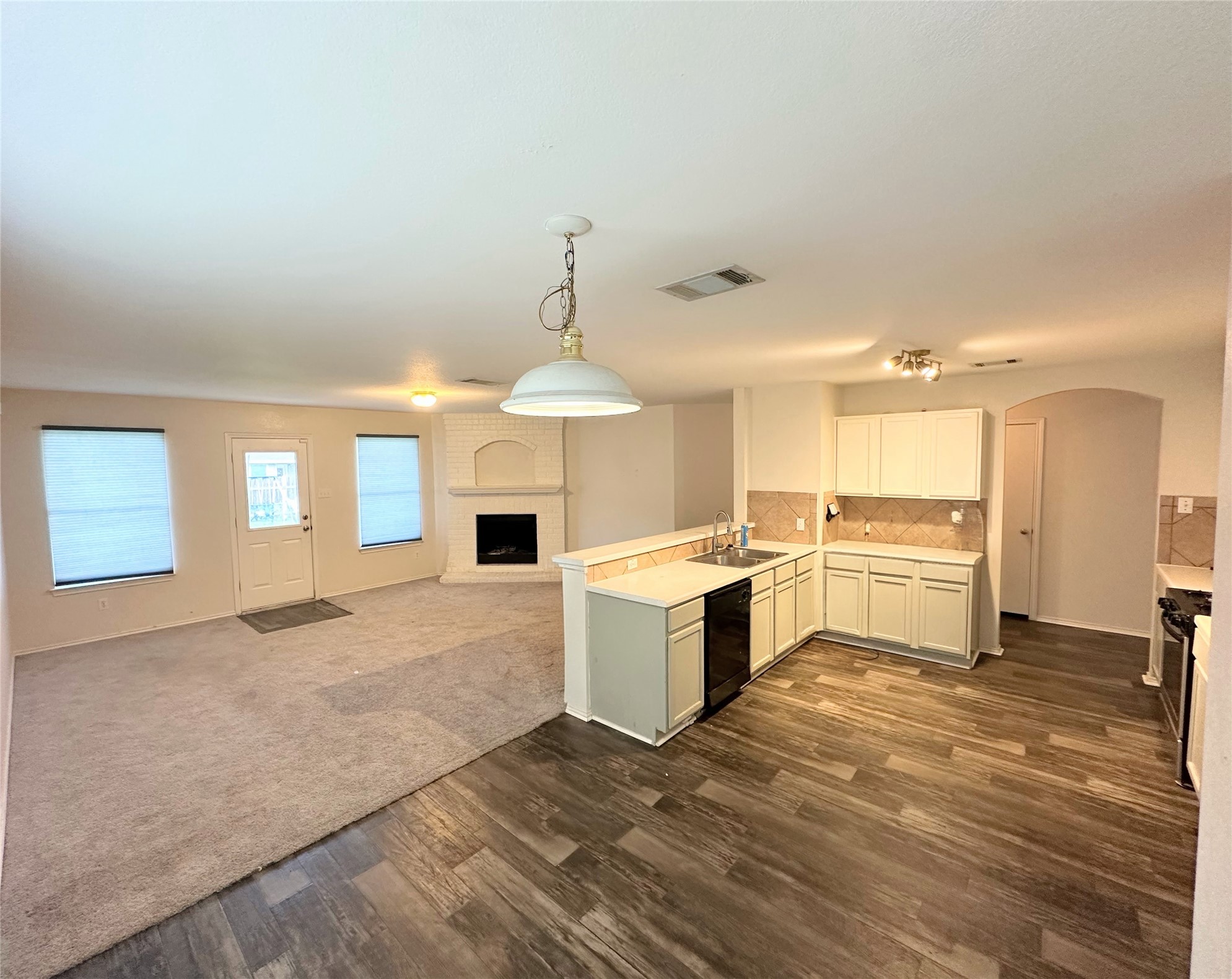 12929 Waynespur Lane Elgin, TX 78621 - Photo 6 of 20 Open concept living area featuring a kitchen with white cabinetry and a tile backsplash, wood-look flooring, and a carpeted living space with a fireplace